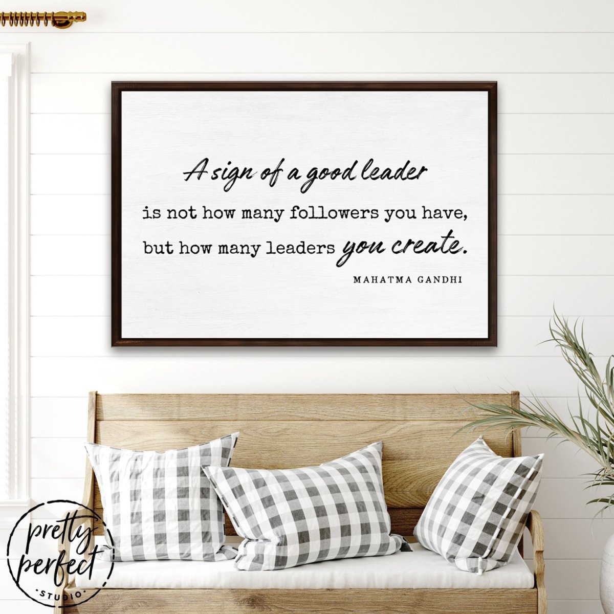 a sign of a good leader canvas wall art with walnut frame featuring Mahatma Gandhi leadership quote above rustic bench with neutral pillows