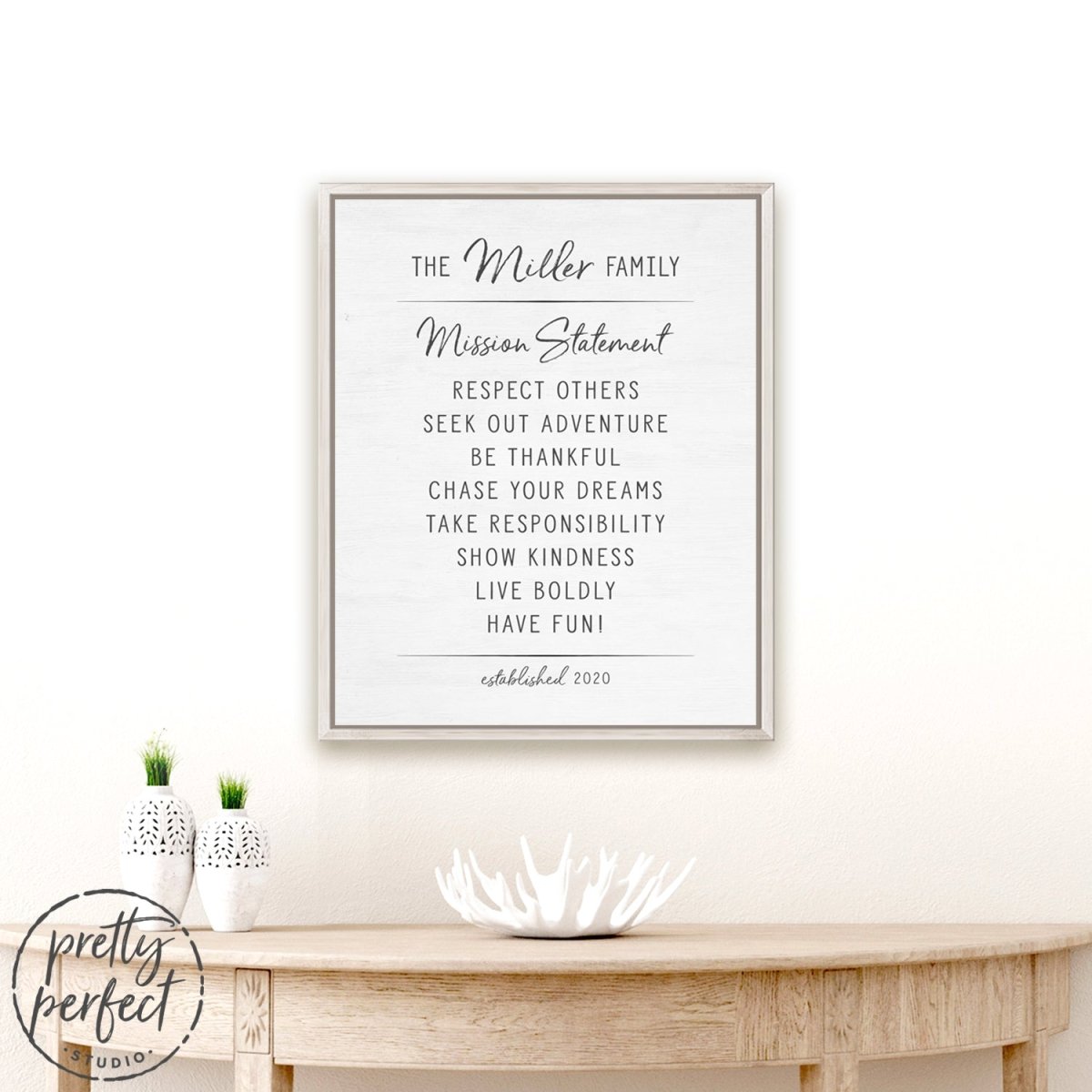 personalized family mission statement sign with rustic white frame displayed above wooden table in minimalist home decor