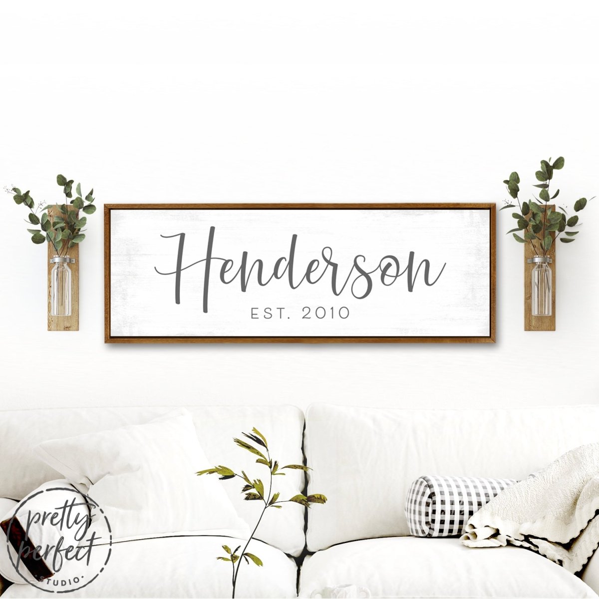 Personalized last name sign Henderson est 2010 farmhouse style custom family name wall decor above couch with rustic wood frame and greenery accents
