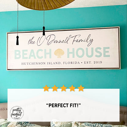 personalized beach house sign with family name, custom coastal wall art with shell design and location, beach home decor above bed, seaside family name sign for vacation home, customer review photo showing framed beach house sign in bedroom