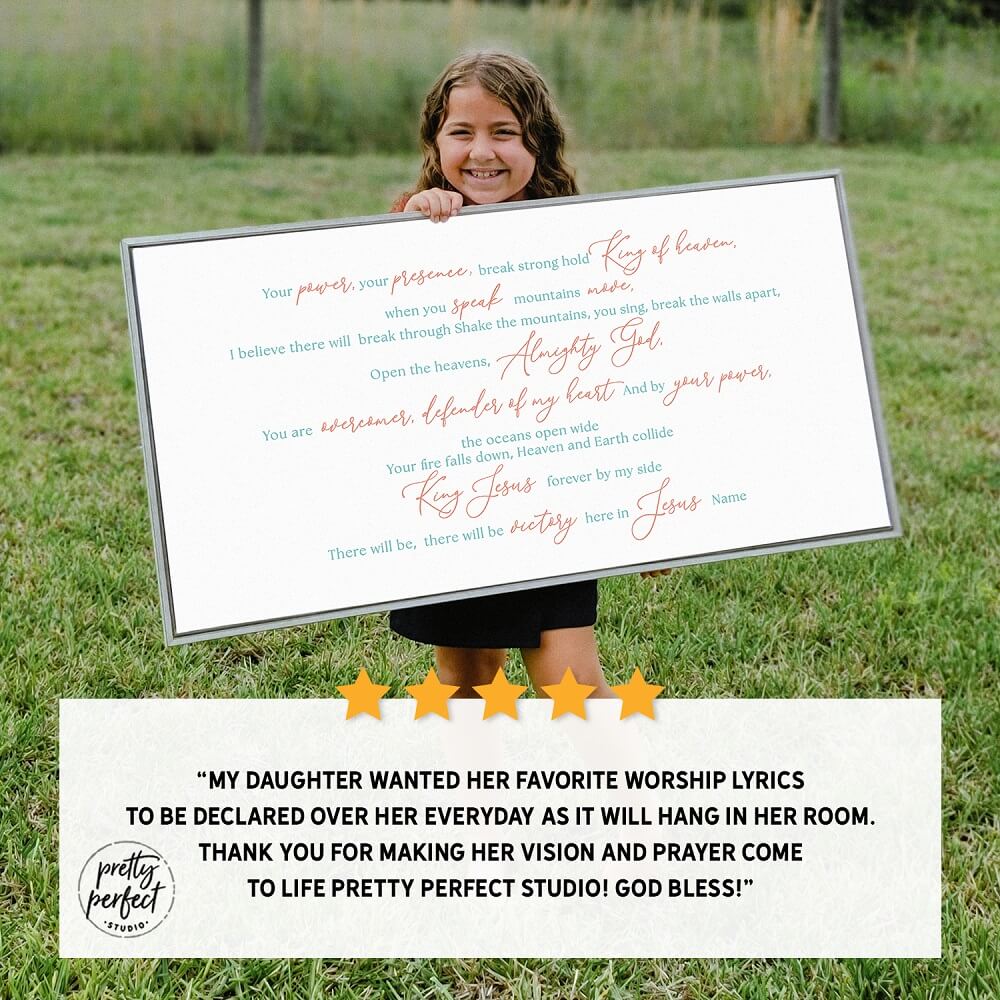 Child holding a framed print of worship lyrics in a grassy outdoor setting