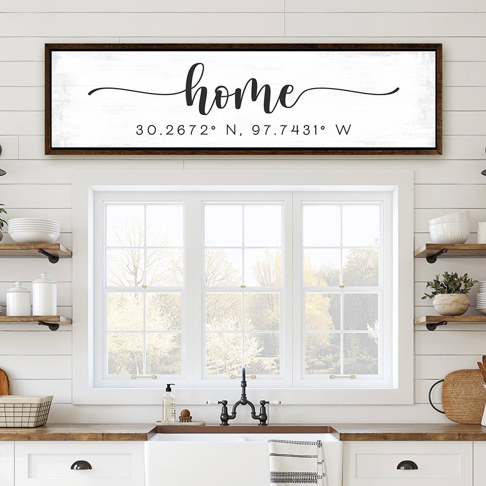 personalized home coordinates sign in wooden frame above bright farmhouse kitchen window with white decor
